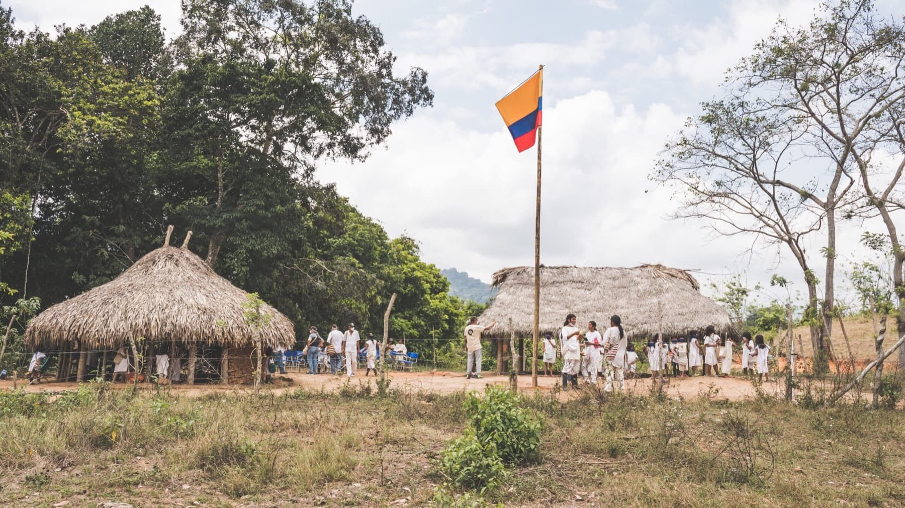 A Kogui community gathered between palm-leaf huts under the flag of Colombia